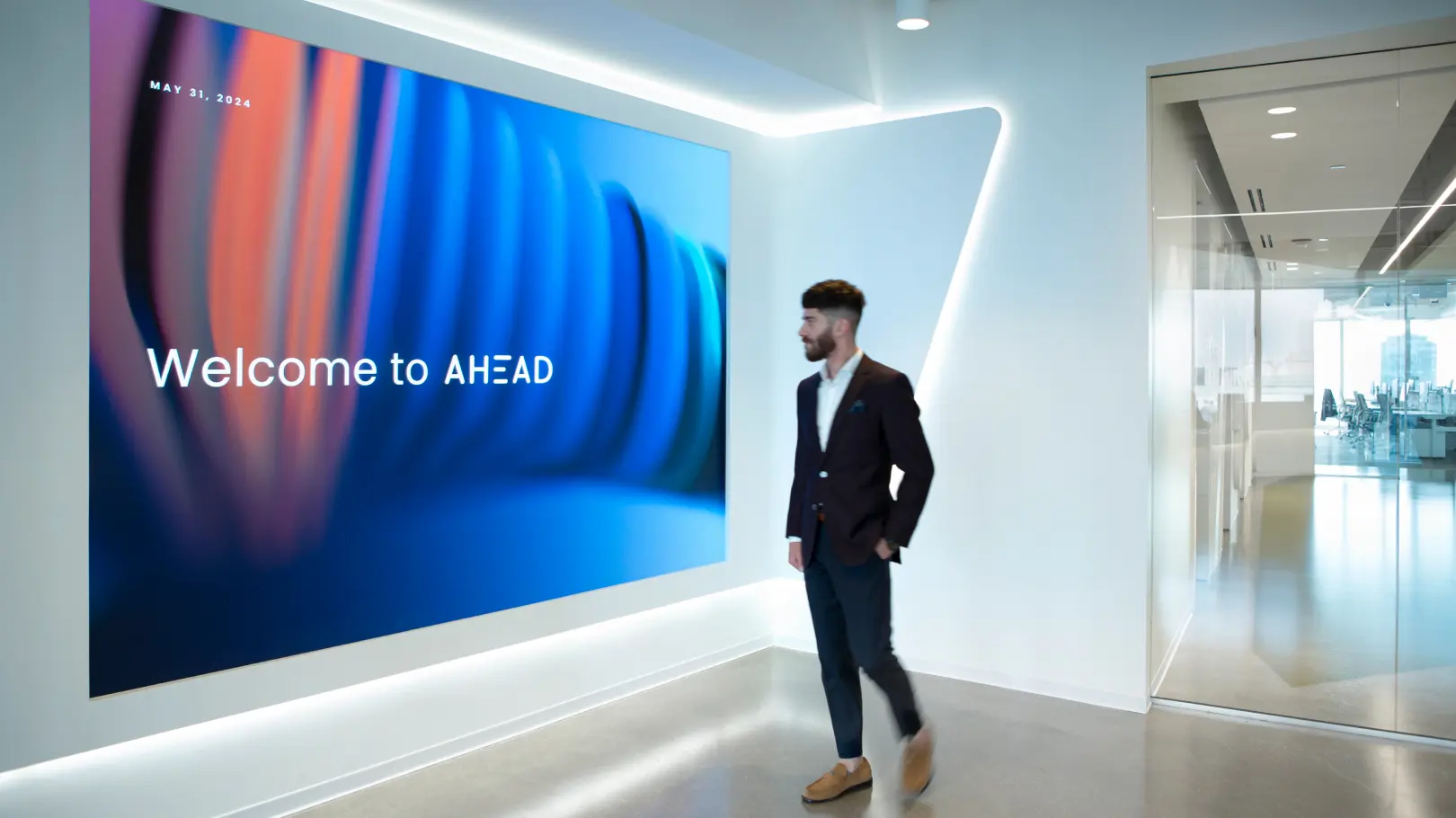 A person in a suit walking in front of the AHEAD Welcome Wall