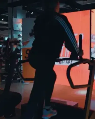 Woman on treadmill backlit with the orange glow of a large LED display