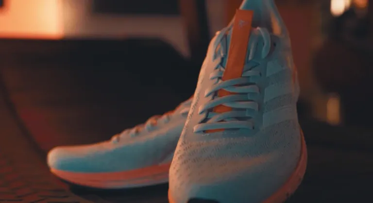 Close-up of adidas running shoes positioned on treadmill with low light orange color glow