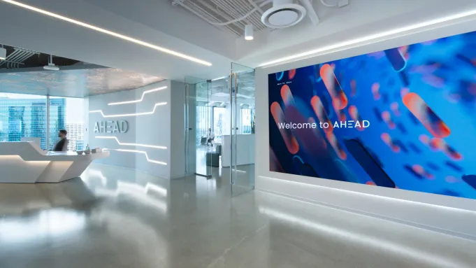 AHEAD corporate lobby, with a person sitting in a desk on the left, glass doors, and the AHEAD Welcome Wall on the right