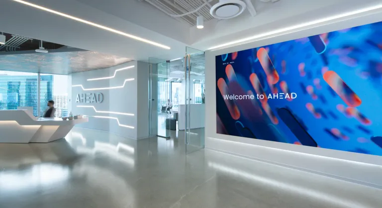 AHEAD corporate lobby, with a person sitting in a desk on the left, glass doors, and the AHEAD Welcome Wall on the right