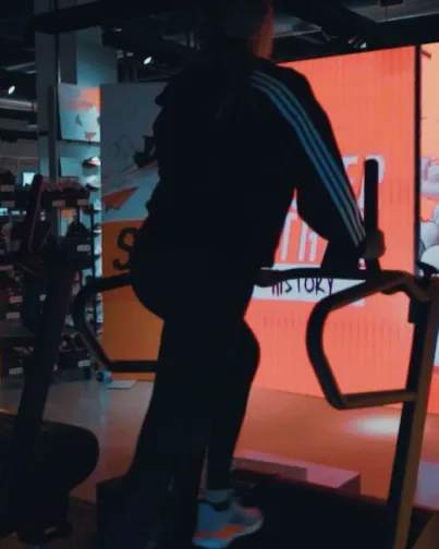 Woman on treadmill backlit with the orange glow of a large LED display