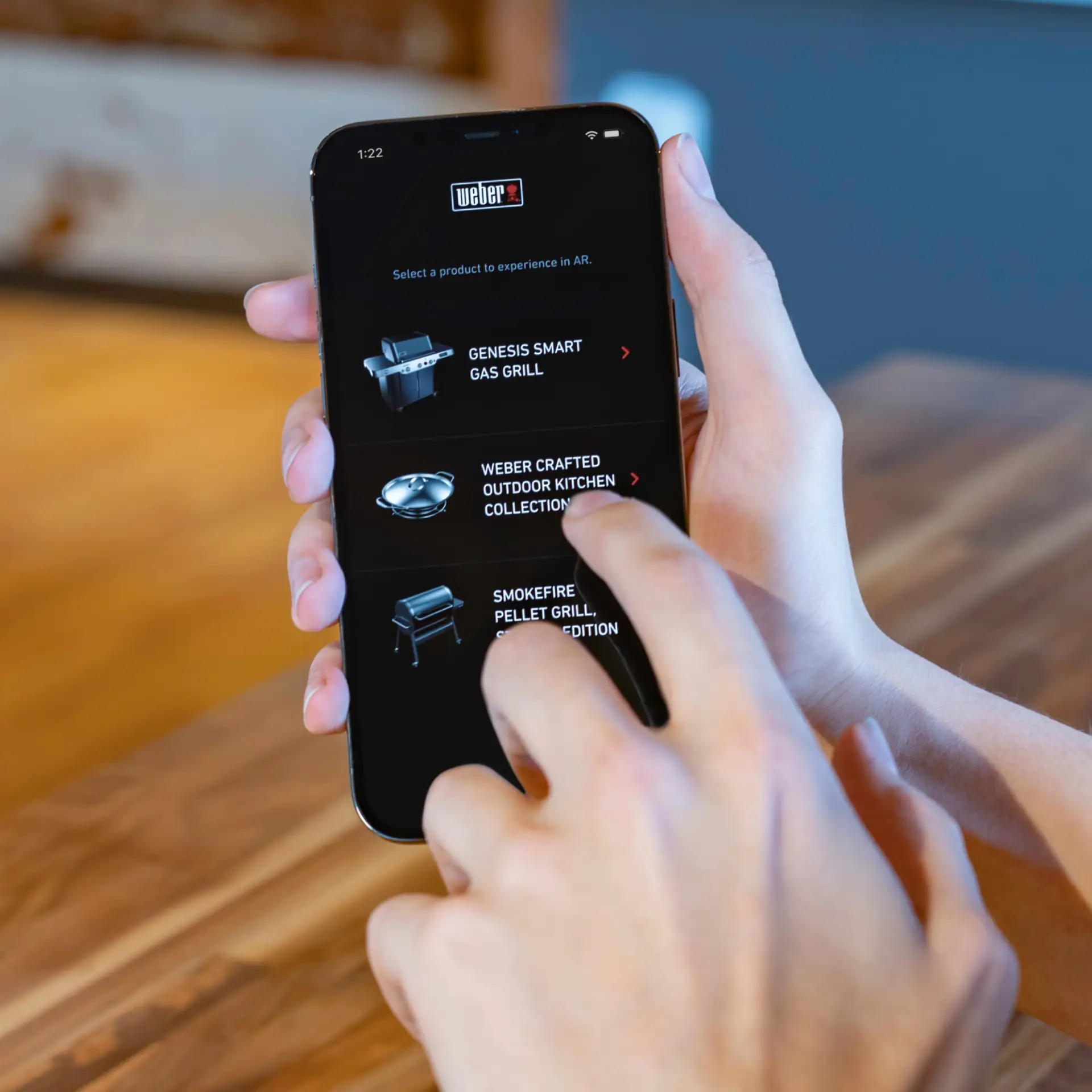 Right hand holding phone with Weber AR homepage open and left hand raised to touch in to application