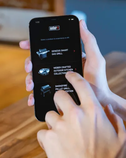 Right hand holding phone with Weber AR homepage open and left hand raised to touch in to application