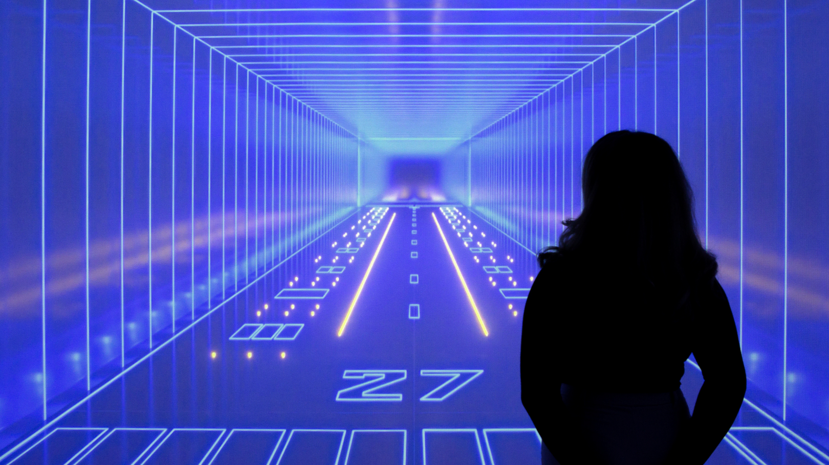 The silhouette of a woman in front of a bright blue image depicting a fantastical neon runway inside an endless tunnel