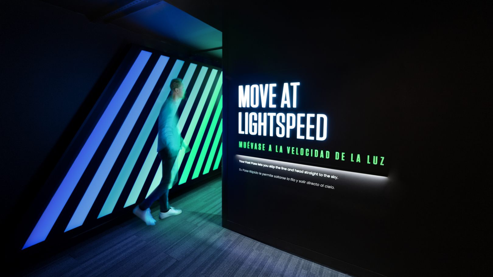 A person entering the Fast Pass line. Text on the wall says "Move at Lightspeed". Wall is glowing blue and green.