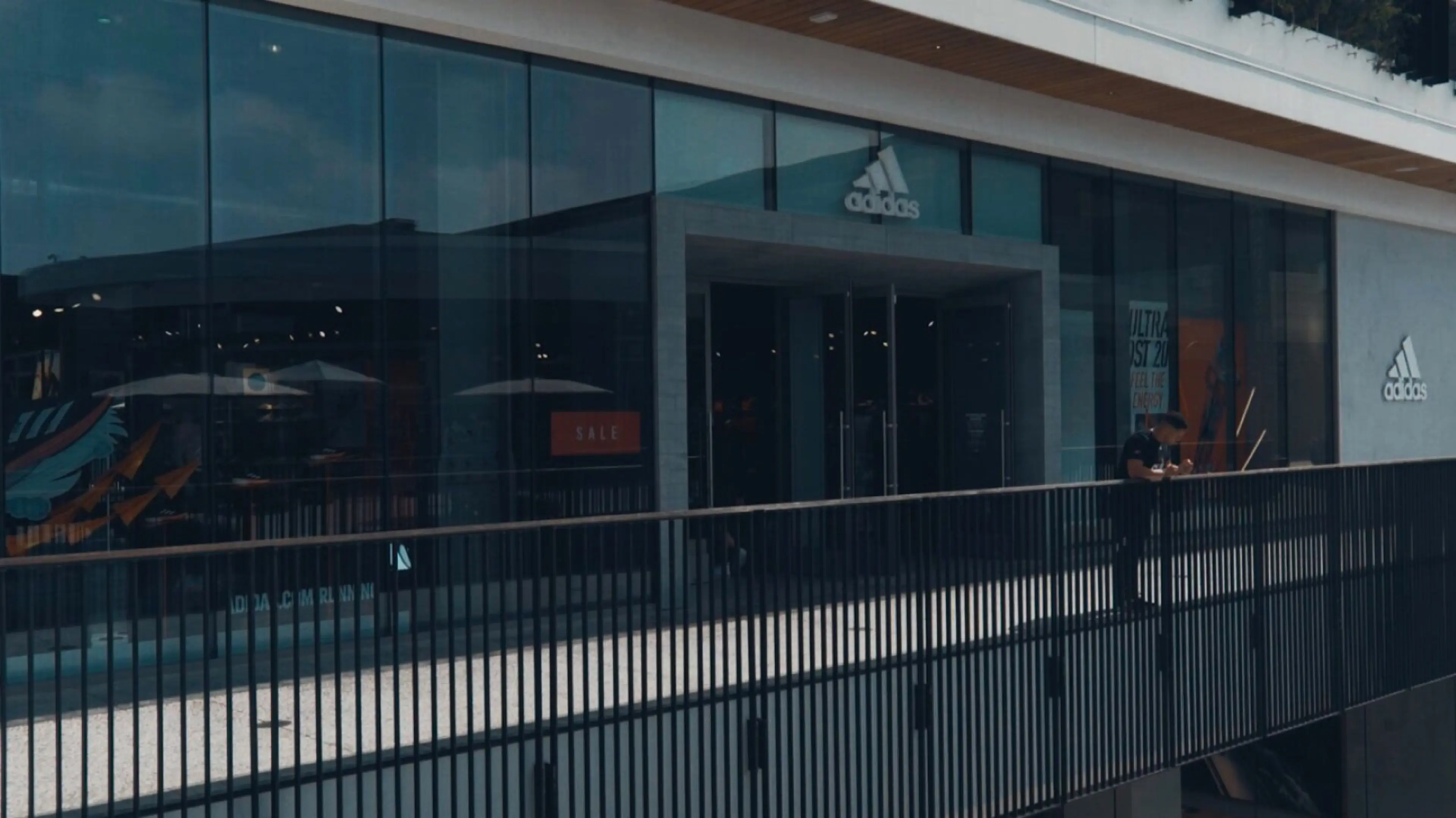 Adidas storefront window on the second floor of an outdoor mall in California with man leaning against the railing