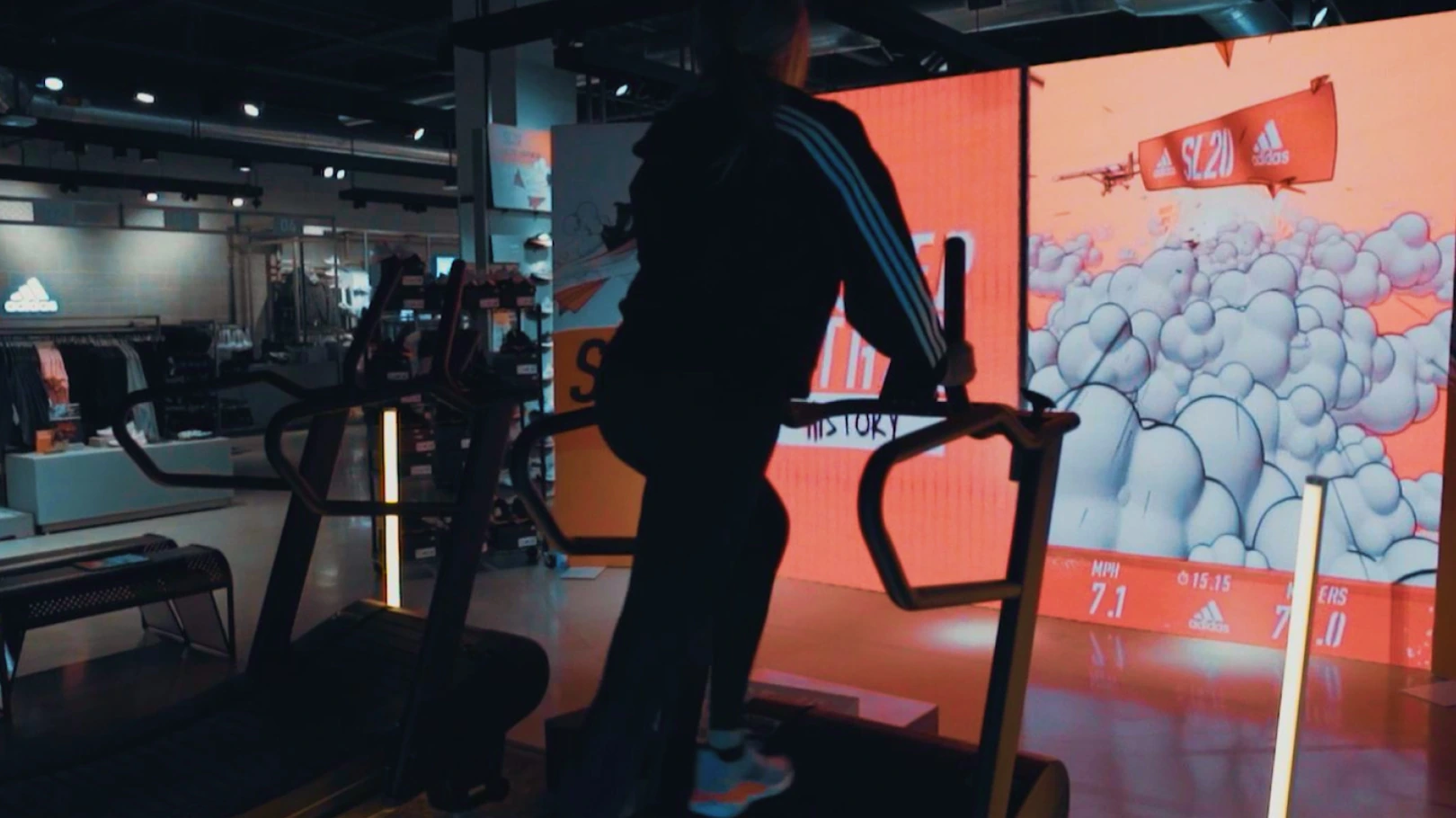 Person on treadmill backlit with the orange glow of a large LED display