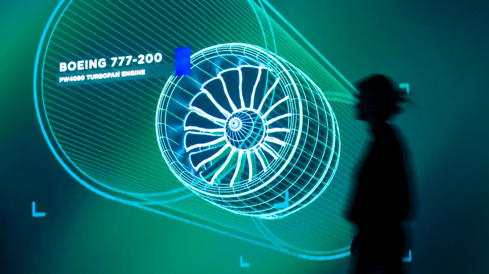 Woman in silhouette in front of a large green glowing image of an airplane engine CAD drawing